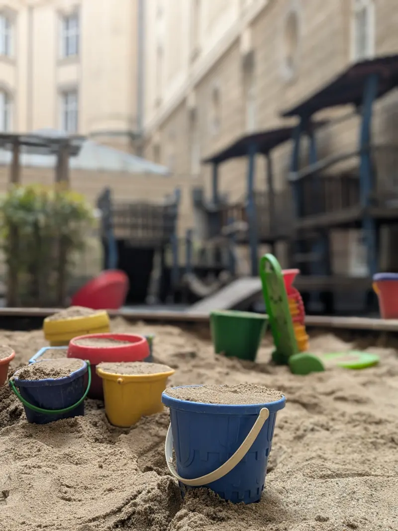 Sandkasten mit bunten Eimern und Förmchen im Innenhof, dahinter die historische Fassade.